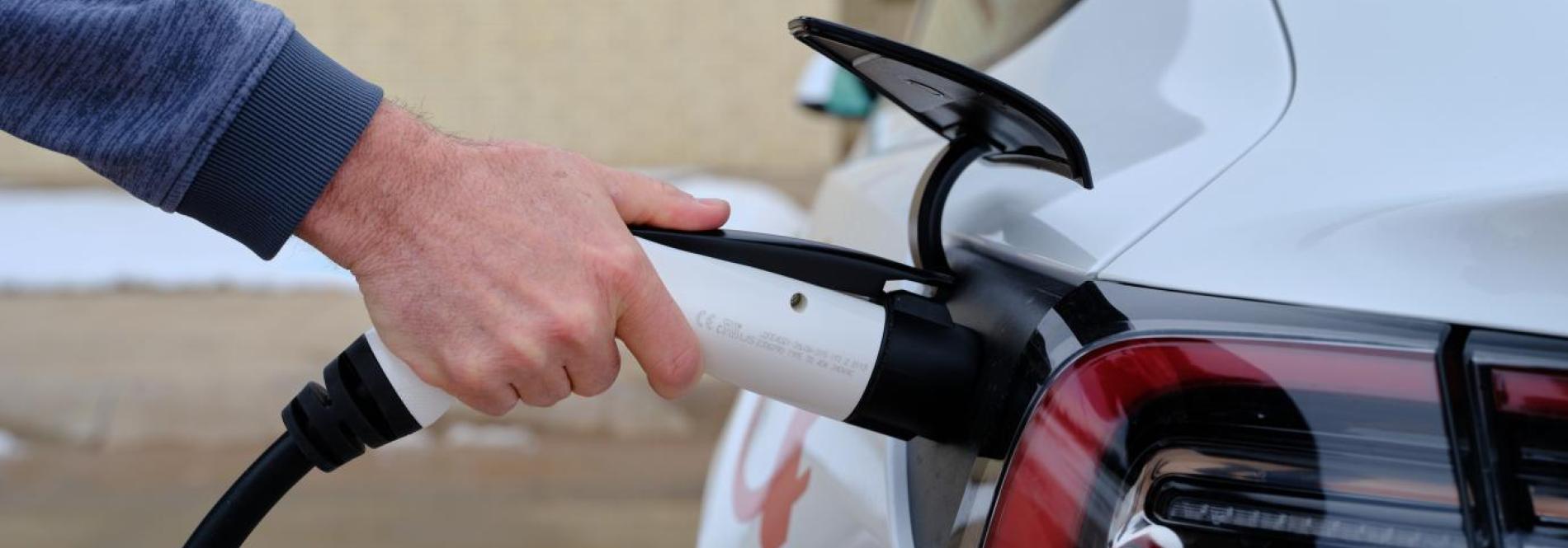 A hand plugging a charger into an EV