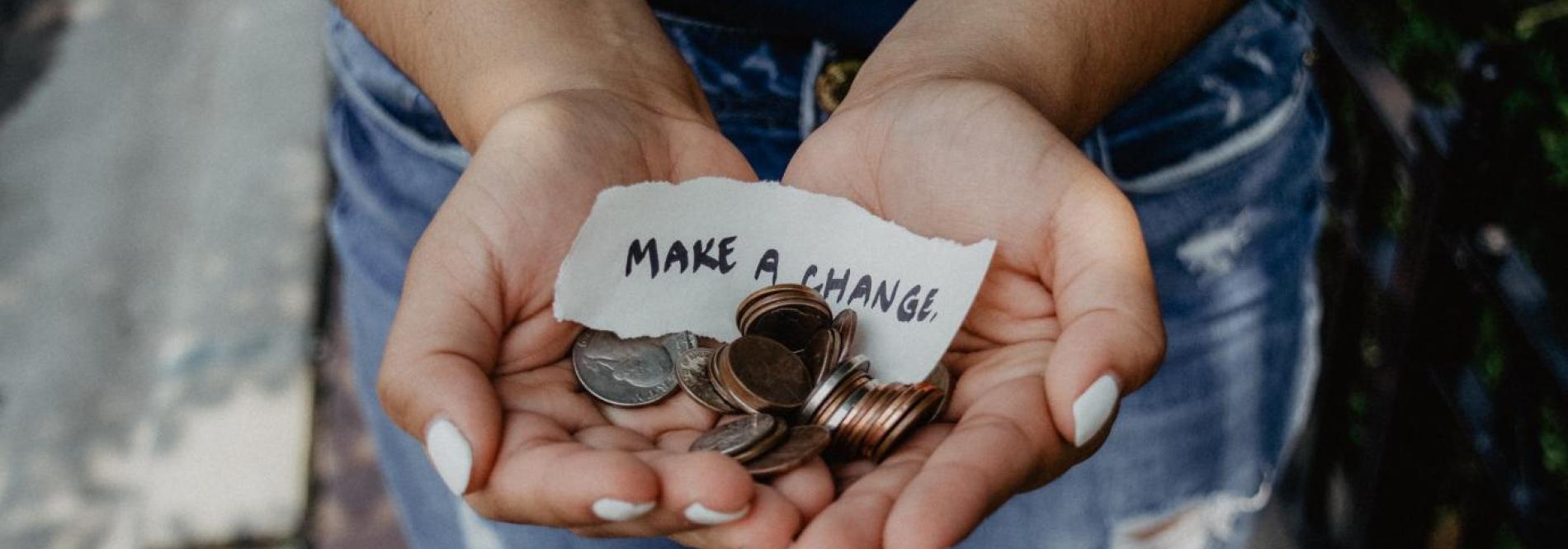 Hands holding note that says make a change with some change in quarters, dimes, and nickels